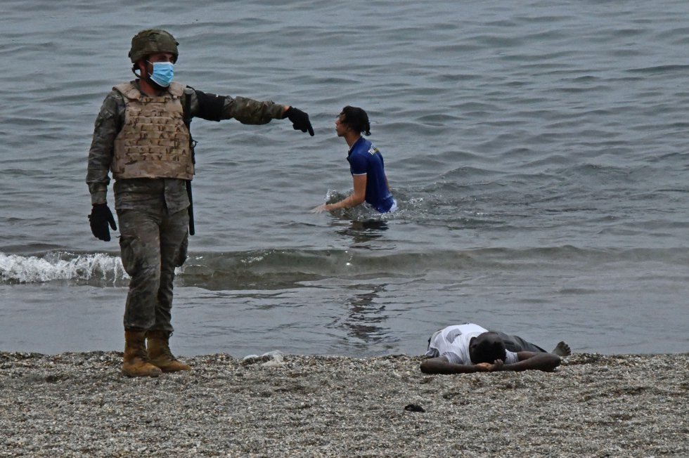Un soldado del Ej&eacute;rcito de Tierra avisa a los sanitarios para que acudan a asistir a un joven que permanece tumbado en la arena. La entrada de 6.000 personas de forma irregular en un solo d&iacute;a es un acontecimiento in&eacute;dito en Espa&ntilde;a. Ni en los momentos de m&aacute;s presi&oacute;n migratoria se han alcanzado cifras similares. El r&eacute;cord m&aacute;s reciente se bati&oacute; el fin de semana del 7 y 8 de noviembre en Canarias, cuando entraron en un solo d&iacute;a 1.500 personas y ese fin de semana acabaron desembarcando casi 2.200 migrantes.
