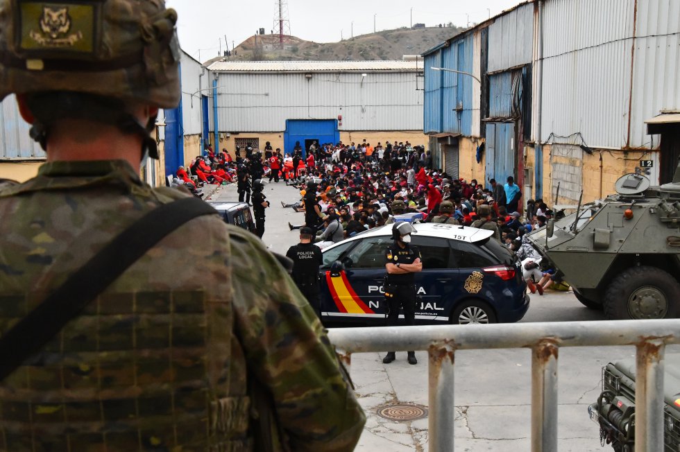 Agentes de la Polic&iacute;a Nacional y militares vigilan a cientos de inmigrantes tras su llegada este martes a Ceuta.