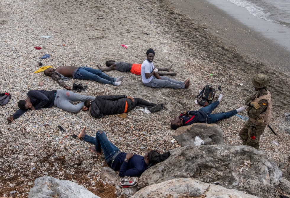 Espa&ntilde;a ha devuelto ya a 4.000 personas a Marruecos, seg&uacute;n el Ministerio del Interior. El ministro Fernando Grande-Marlaska ha asegurado que entre ellos no hay menores. Mientras, Marruecos ha desplegado este martes antidisturbios en la frontera para frenar la entrada de migrantes a Ceuta. En la imagen, un soldado custodia a varios j&oacute;venes inmigrantes, algunos de ellos heridos, en la playa del Tarajal, en la frontera de Ceuta.