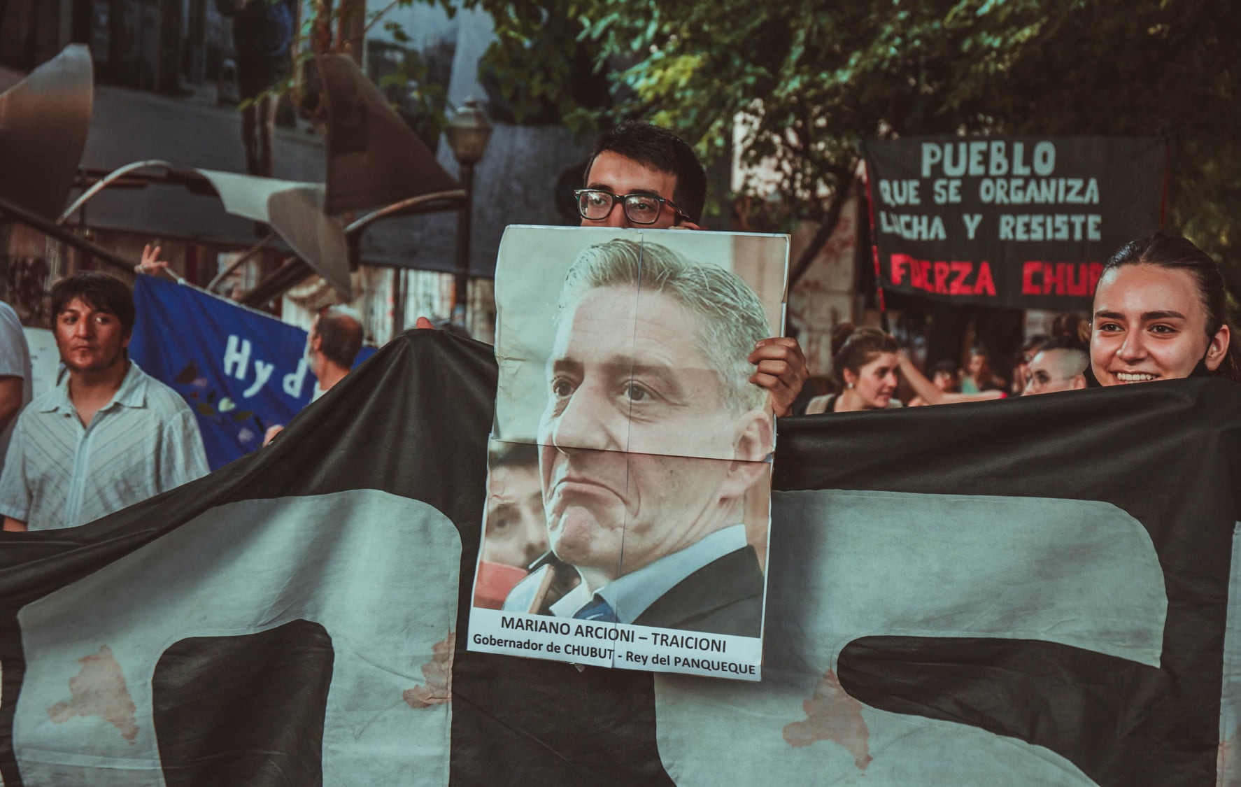 Puede ser una imagen de 4 personas, personas de pie, multitud, al aire libre y texto que dice "PUEBLO QUE SE ORGANIZA LICHA RESISTE FIRZA CHUP MARIANO ARCIONI TRAICIONI Gobernado de CHUBUT Rey elP ANQUEQUE"